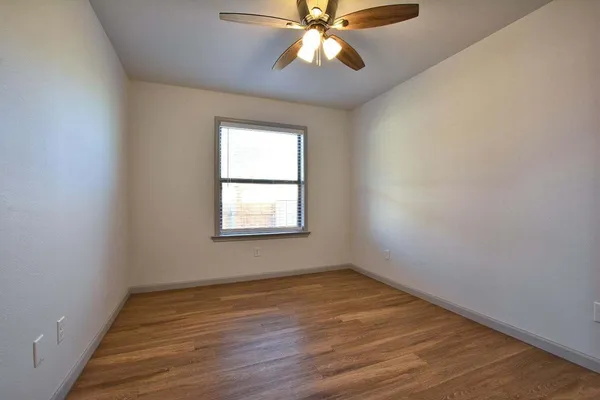 an empty room with wooden floor fan and windows