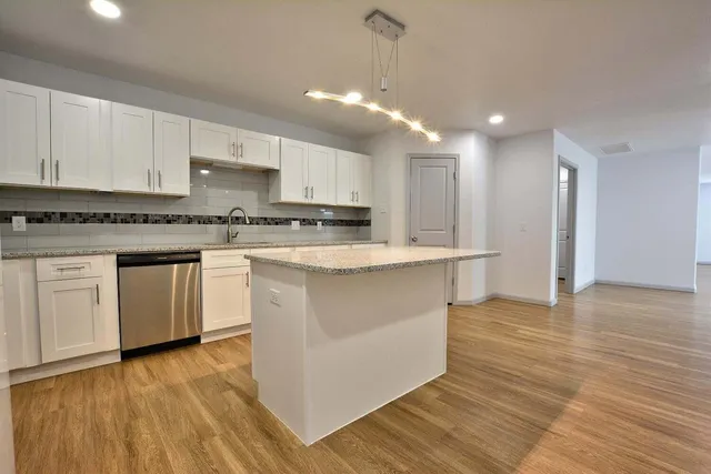 a kitchen with stainless steel appliances granite countertop a stove top oven a sink dishwasher and a refrigerator with wooden floor