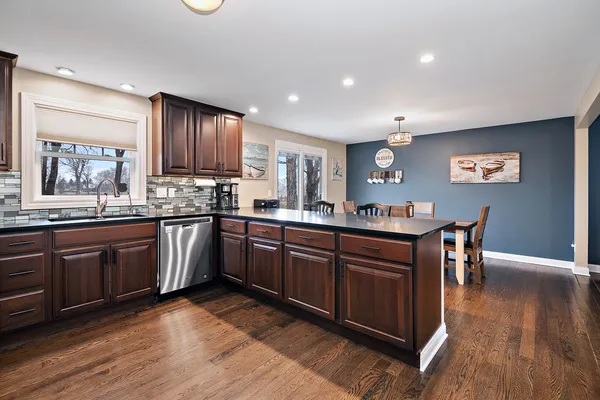 a kitchen with stainless steel appliances granite countertop wooden cabinets a sink a stove a dining table and chairs