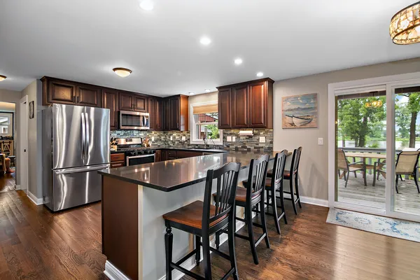 a kitchen with stainless steel appliances granite countertop a refrigerator a stove a dining table and chairs with wooden floor