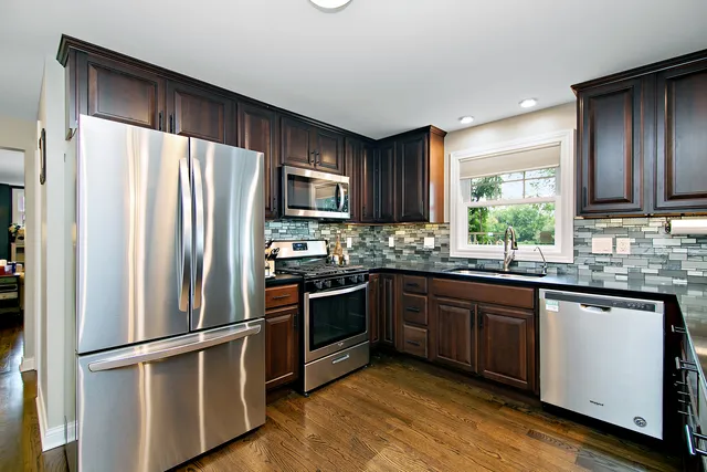 a kitchen with stainless steel appliances granite countertop a refrigerator a stove a dining table and chairs with wooden floor