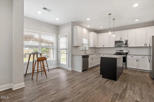 a kitchen with kitchen island granite countertop wooden floors stainless steel appliances a sink and a window
