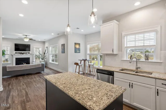 a kitchen with kitchen island granite countertop wooden cabinets a sink dishwasher and a stove with wooden floor
