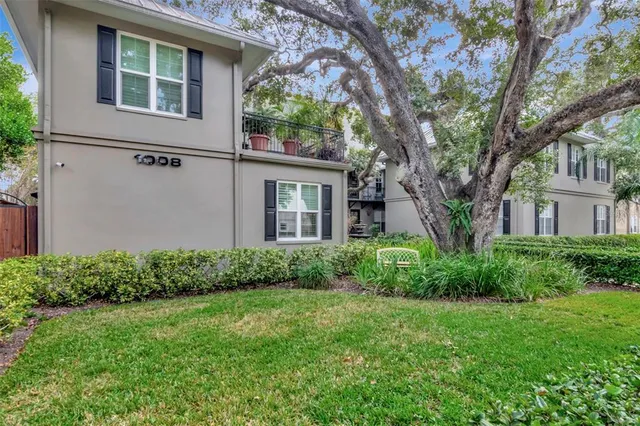 a view of a brick house with a small yard plants and large tree