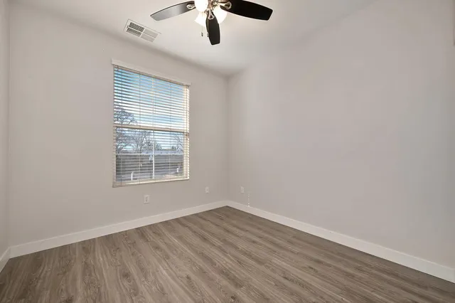 an empty room with wooden floor fan and windows