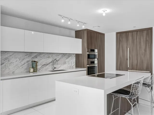 a kitchen with stainless steel appliances a sink a stove a refrigerator with white cabinets and wooden floor