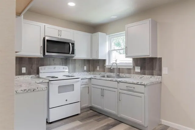 a kitchen with granite countertop white cabinets stove top oven and sink