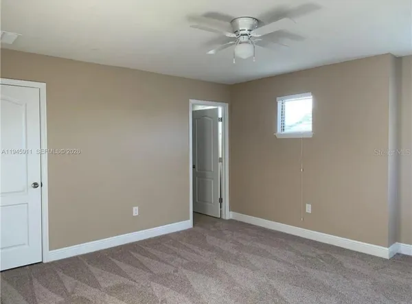 an empty room with chandelier fan and windows