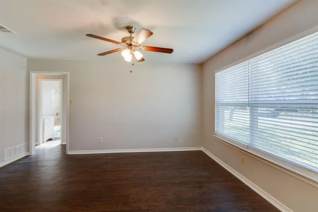 an empty room with wooden floor fan and windows