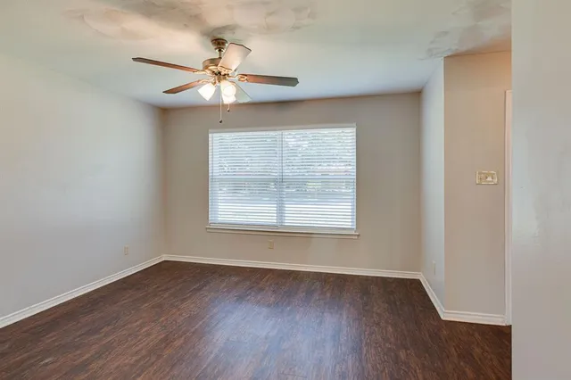 an empty room with wooden floor chandelier fan and windows