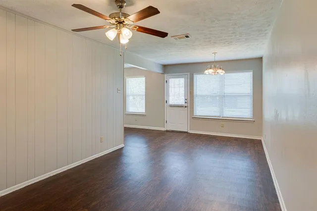 an empty room with wooden floor chandelier fan and windows