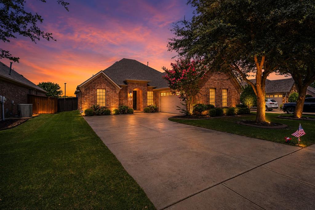 1995 Verde Court Allen, TX 75013 - Photo 30 of 30 Brick exterior residence featuring integrated garage, mature trees, and landscaped shrubbery with exterior illumination