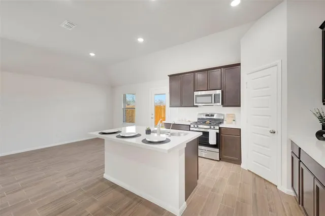 a kitchen with stainless steel appliances granite countertop a stove top oven a sink dishwasher and a refrigerator with wooden floor