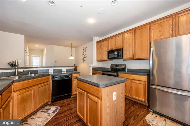 a kitchen with stainless steel appliances granite countertop a stove top oven a refrigerator a sink and dishwasher with wooden floor