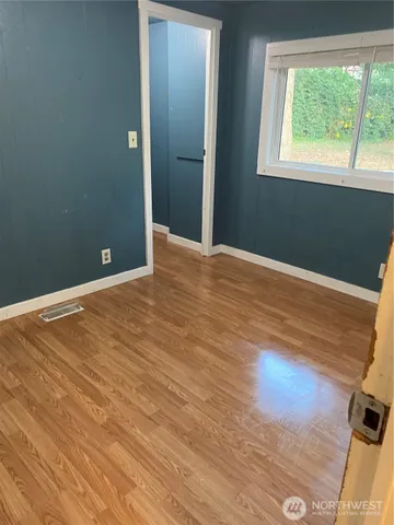 a view of an empty room with wooden floor and a window