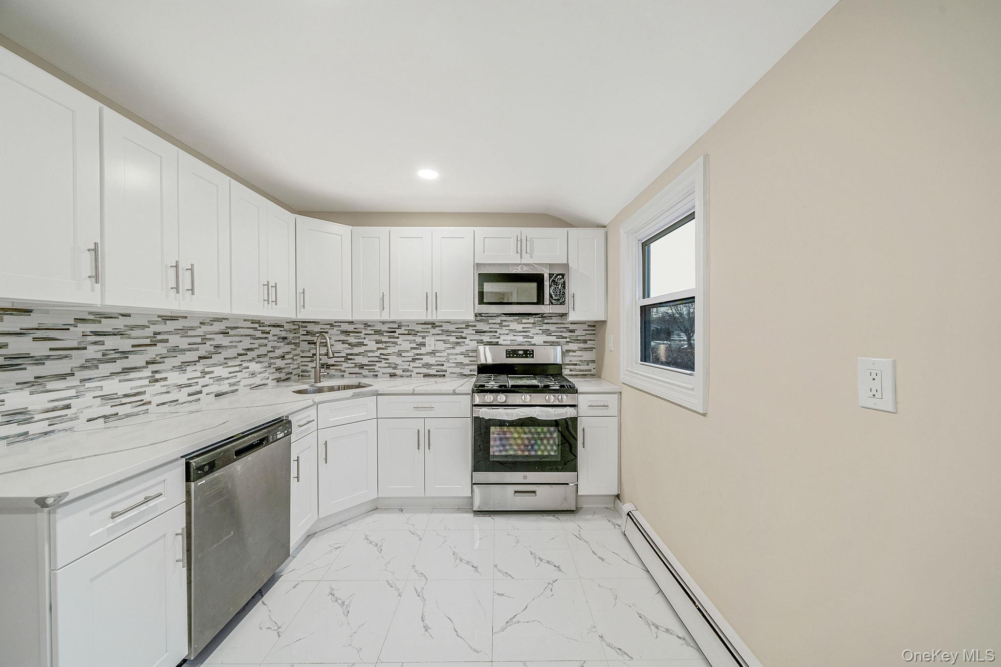 119 Foster Road Ronkonkoma, NY 11779 - Photo 14 of 26 Kitchen featuring appliances with stainless steel finishes, baseboard heating, light marble finish floors, white cabinets, and backsplash