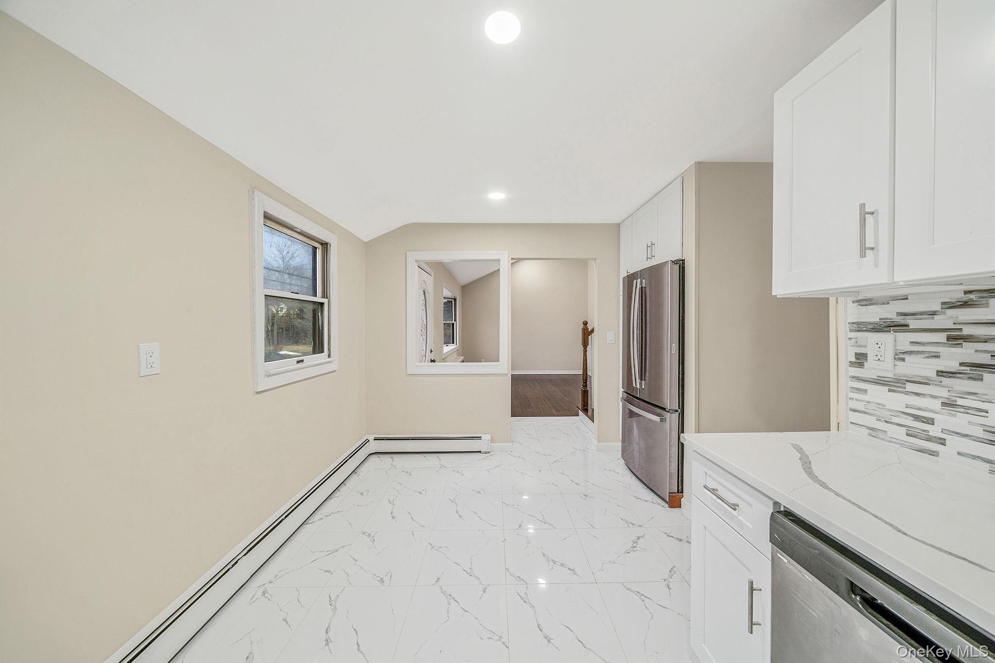 119 Foster Road Ronkonkoma, NY 11779 - Photo 16 of 26 Kitchen with a baseboard heating unit, light stone counters, stainless steel appliances, white cabinetry, and light marble finish flooring