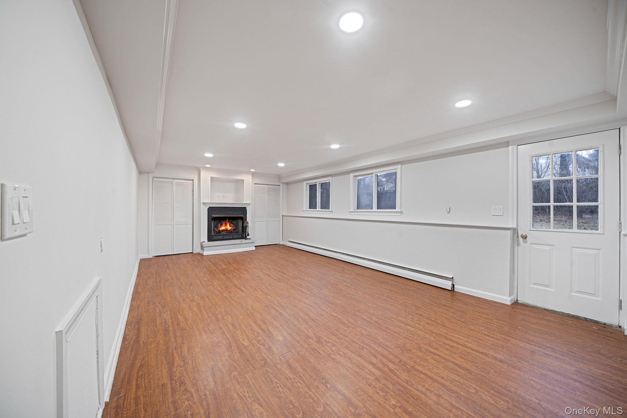 119 Foster Road Ronkonkoma, NY 11779 - Photo 23 of 26 Unfurnished living room featuring a lit fireplace, a baseboard heating unit, light wood finished floors, recessed lighting, and crown molding