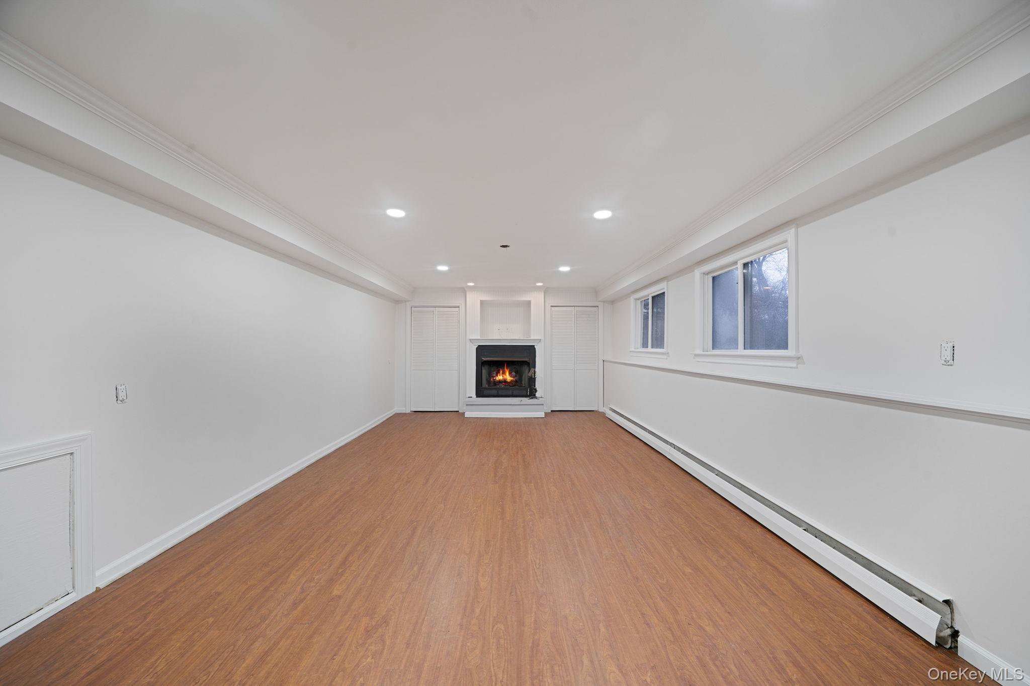 119 Foster Road Ronkonkoma, NY 11779 - Photo 24 of 26 Unfurnished living room with a baseboard heating unit, recessed lighting, a lit fireplace, crown molding, and wood finished floors