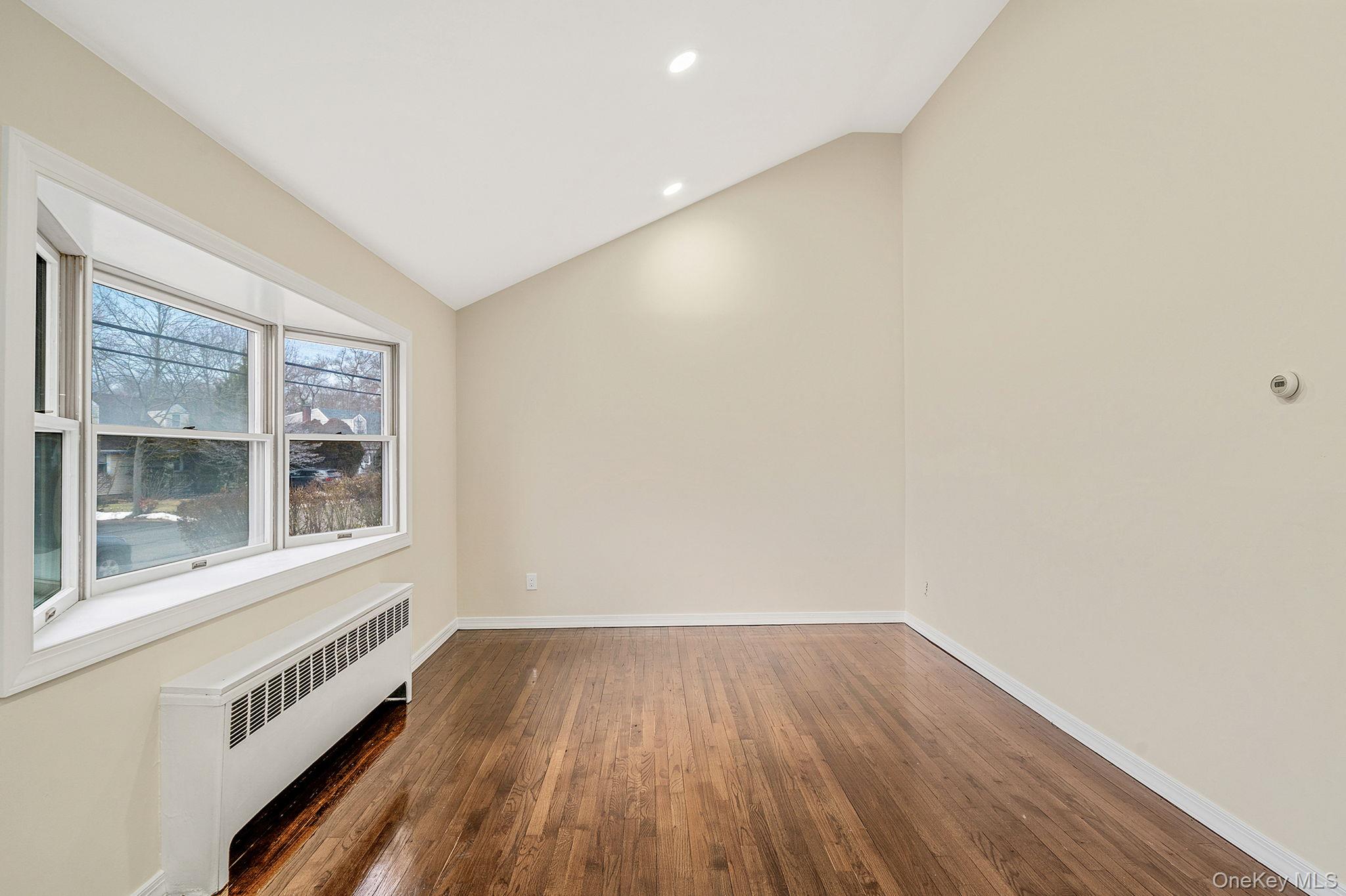 119 Foster Road Ronkonkoma, NY 11779 - Photo 10 of 26 Empty room featuring radiator heating unit, dark wood-style flooring, vaulted ceiling, and recessed lighting