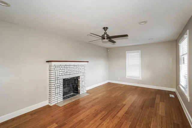 an empty room with wooden floor fireplace and windows
