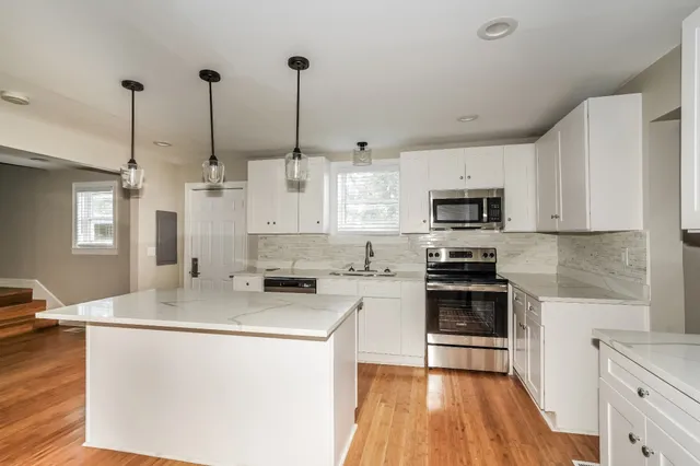 a kitchen with stainless steel appliances kitchen island granite countertop a sink a stove top oven a counter space and cabinets