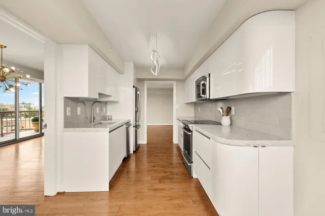 a kitchen with stainless steel appliances granite countertop a refrigerator a sink dishwasher a stove and white countertops with wooden floor