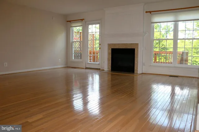 an empty room with wooden floor fireplace and windows