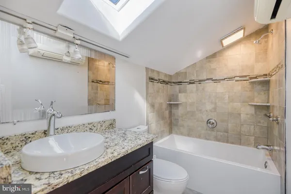 a bathroom with a granite countertop sink a mirror toilet and bathtub