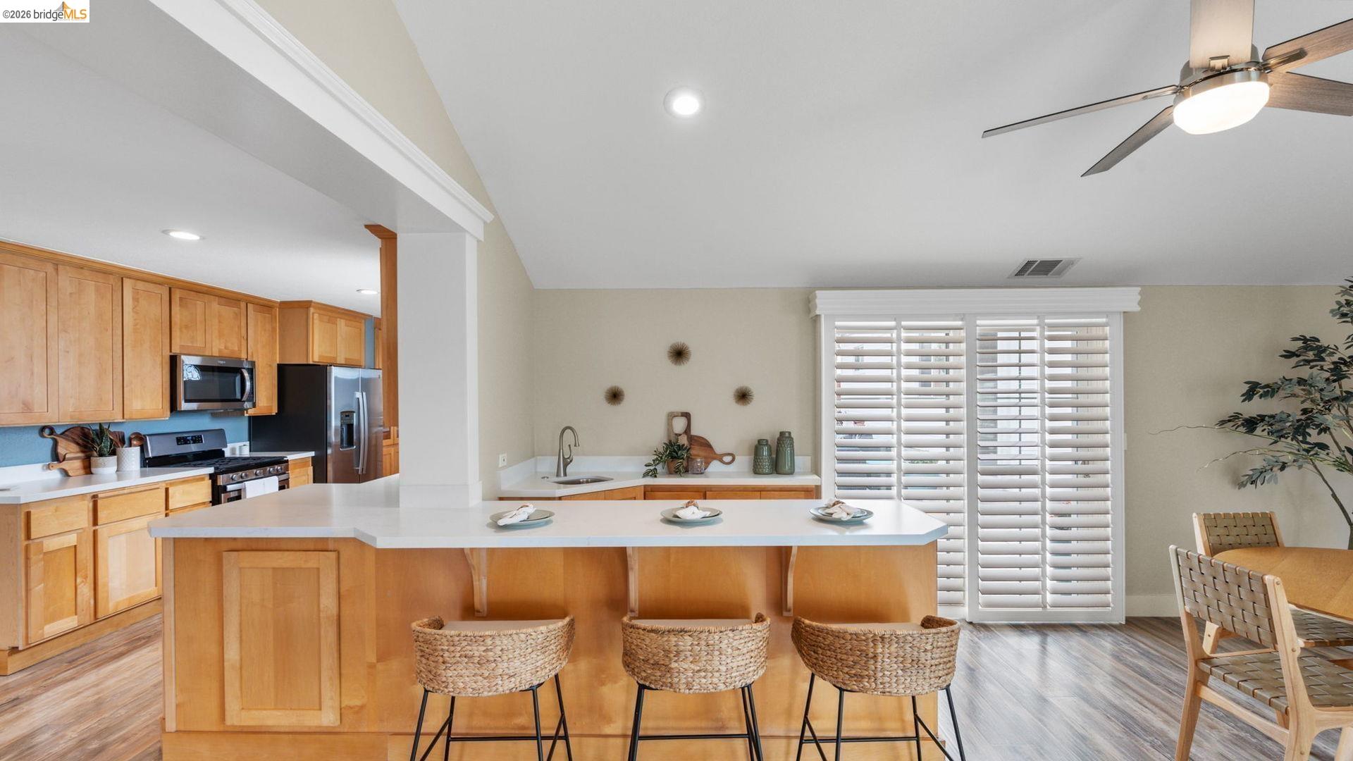 700 Brownstone Road Oakley, CA 94561 - Photo 16 of 58 Open-concept kitchen and dining area featuring light wood-finish cabinetry, stainless steel appliances, a breakfast bar with white countertops, and sliding glass doors with plantation shutters