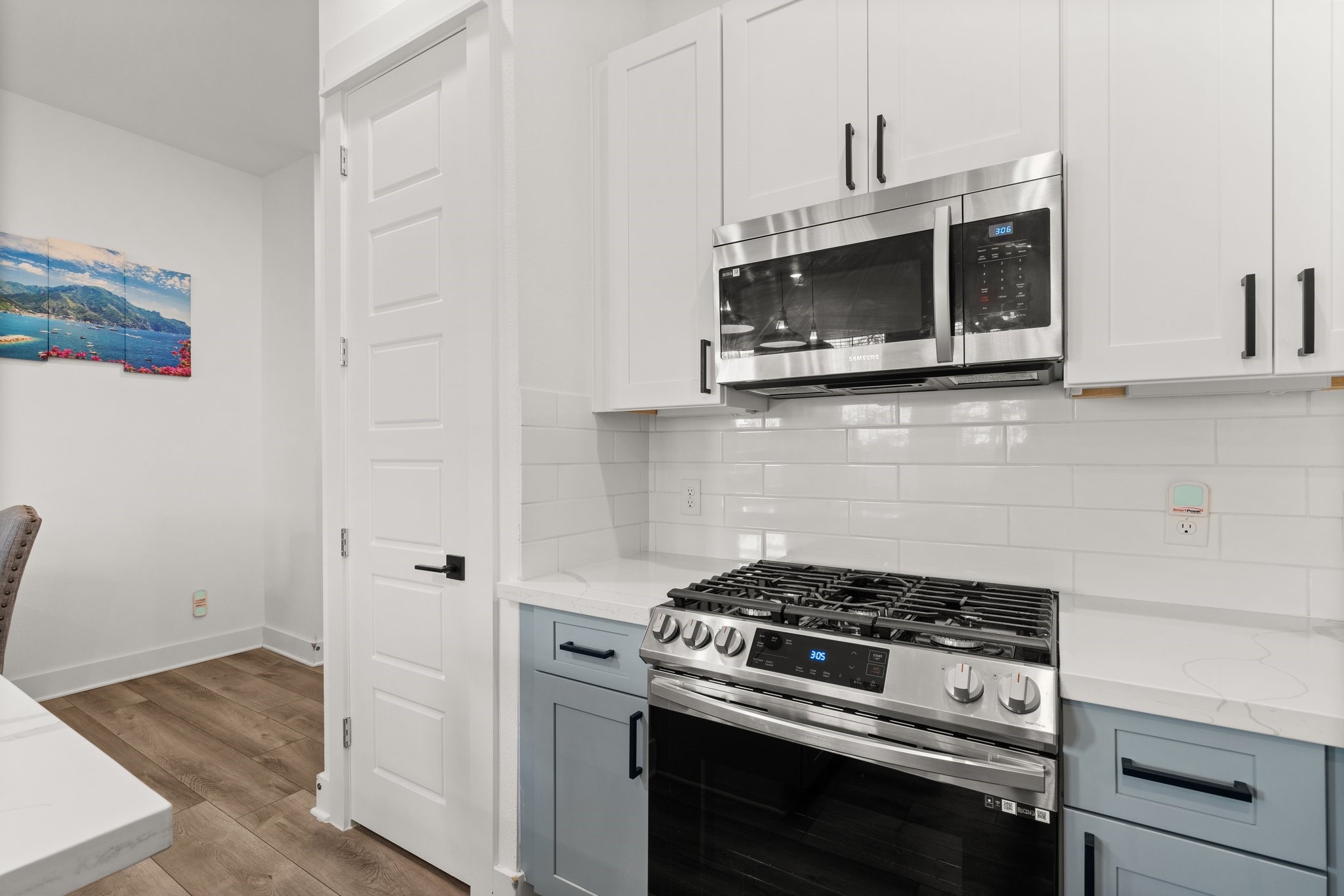 2928 Stevens Street Houston, TX 77026 - Photo 4 of 30 Modern kitchen with stainless steel appliances, including a gas range and microwave. Features white cabinetry, a subway tile backsplash, and light wood flooring.