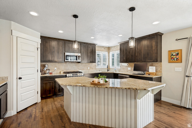Kitchen featuring wood-finish flooring, dark wood cabinetry, a light-toned stone countertop, and a built-in stainless steel microwave