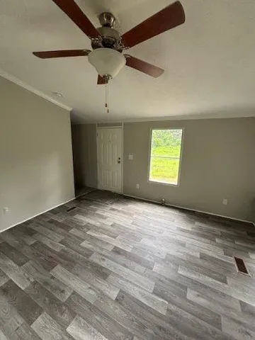 an empty room with wooden floor ceiling fan and windows