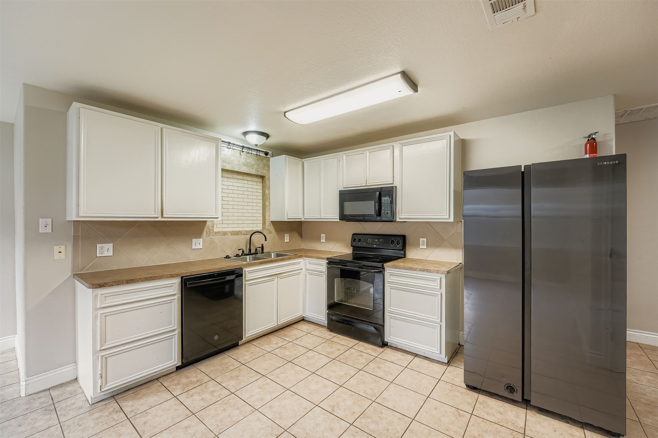 304 South Main Street Elgin, TX 78621 - Photo 12 of 25 Kitchen featuring black appliances, white cabinetry, light countertops, and light tile patterned floors