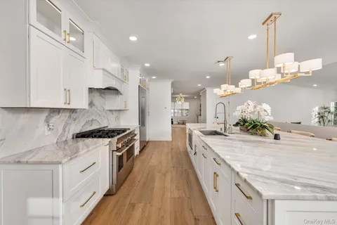 a kitchen with stainless steel appliances kitchen island granite countertop a refrigerator a stove a sink and white cabinets with wooden floor