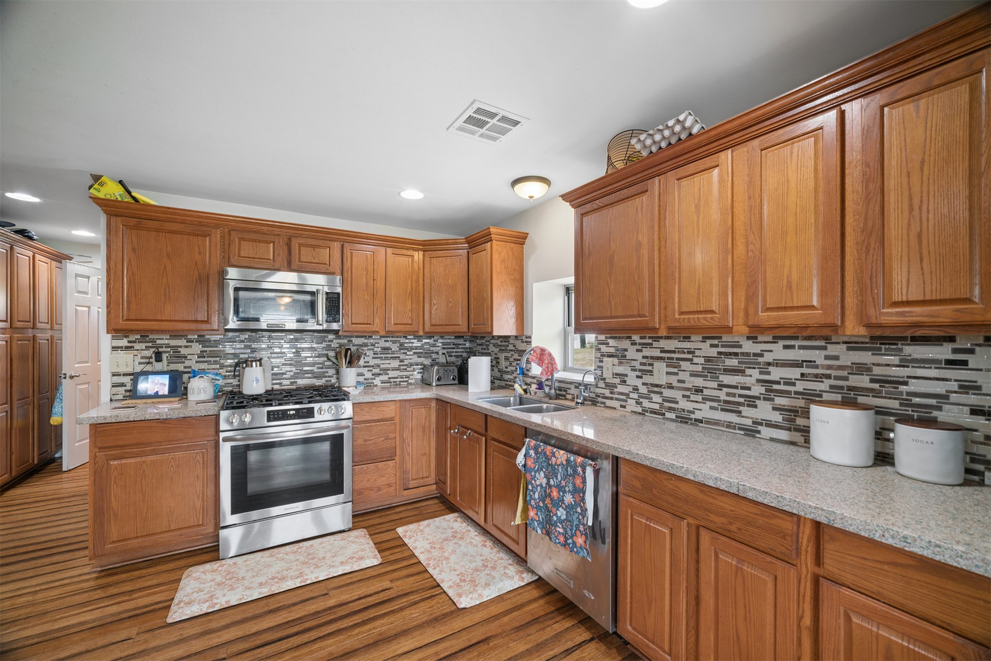 49301 South 360 Road Pawnee, OK 74058 - Photo 9 of 44 Wood-finish flooring with extensive wood cabinetry, stainless steel appliances, speckled countertops, and a mosaic tile backsplash