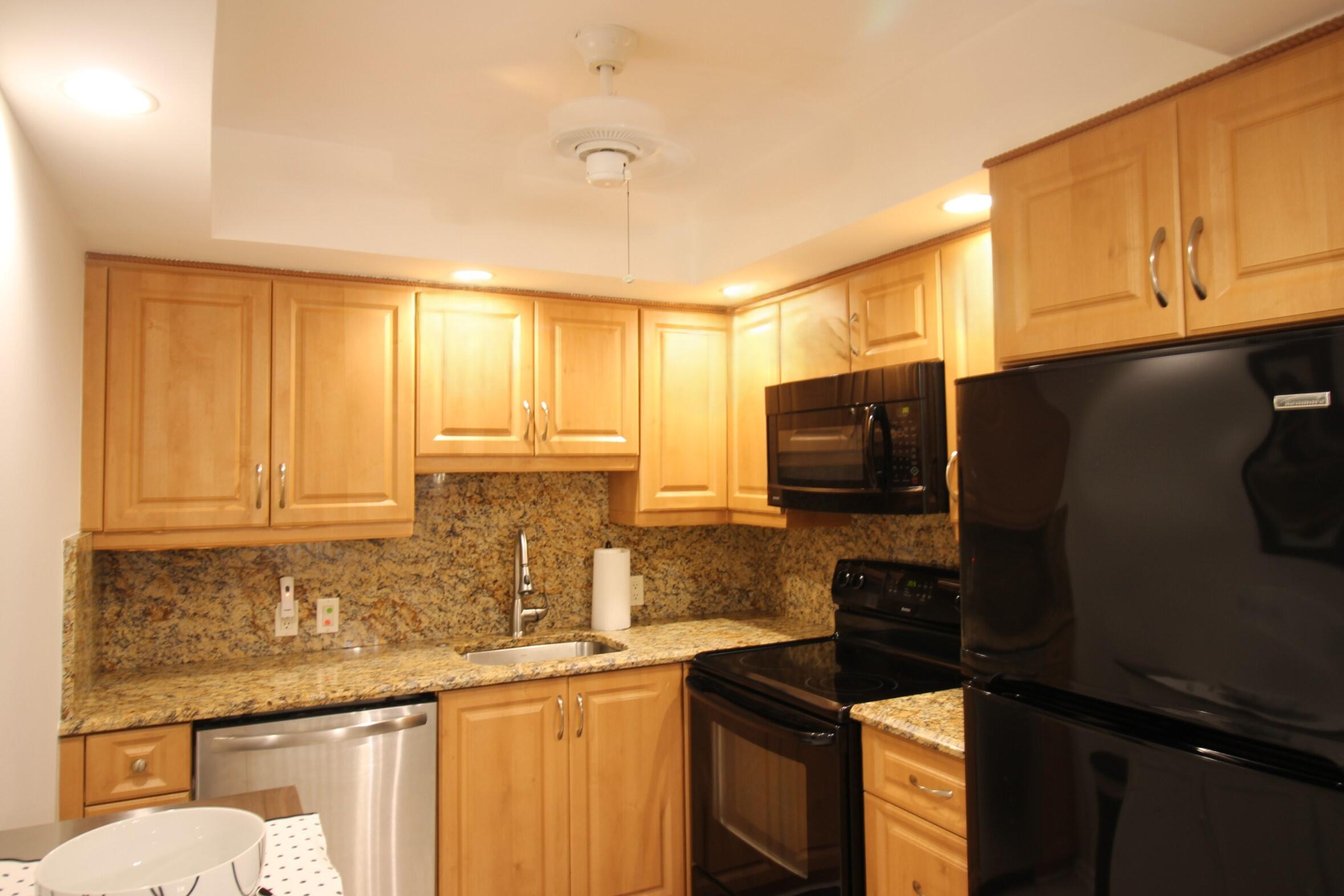 a kitchen with granite countertop a refrigerator a stove top oven cabinets and a sink