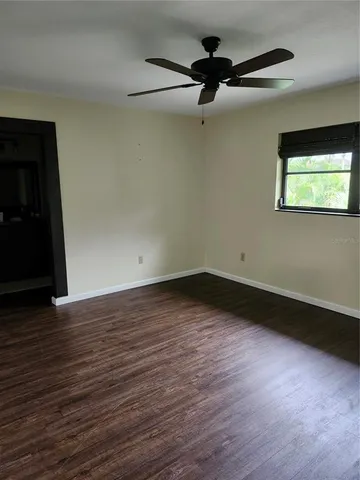 a view of an empty room with wooden floor and a ceiling fan