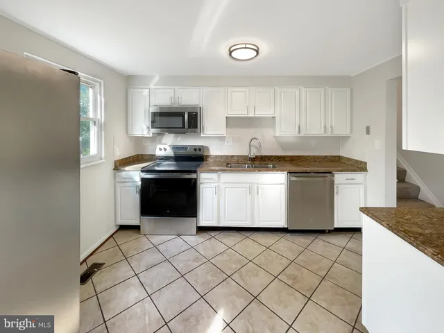 a kitchen with stainless steel appliances granite countertop white cabinets a sink a stove a microwave and a refrigerator