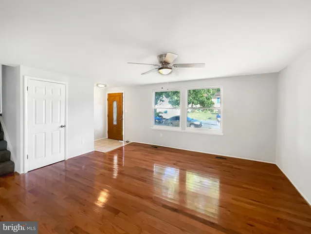 an empty room with wooden floor chandelier fan and windows