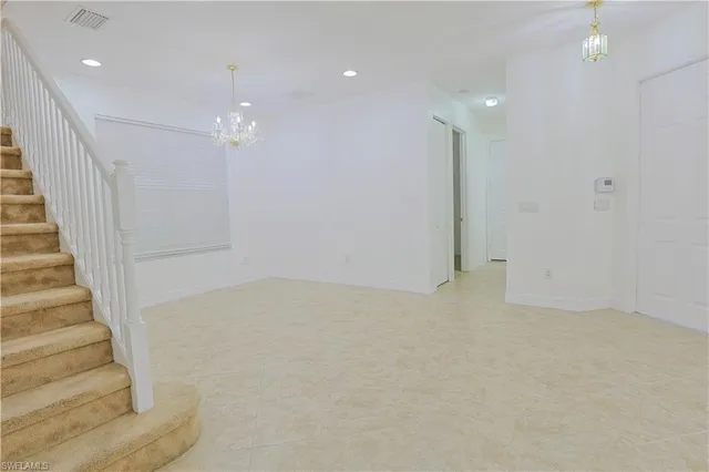 a view of an empty room with stairs and chandelier fan