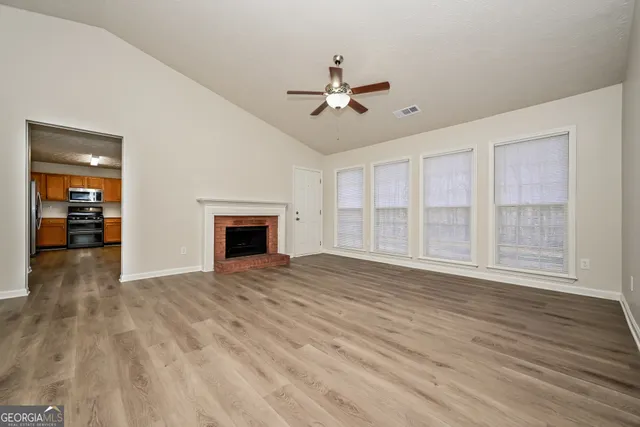 a view of an empty room with wooden floor fireplace and a window
