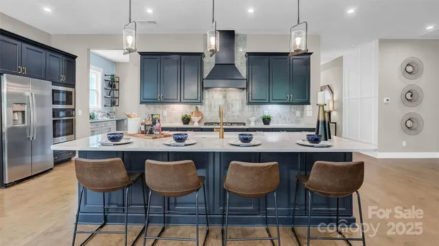 a kitchen with stainless steel appliances granite countertop a sink a stove a refrigerator and chairs