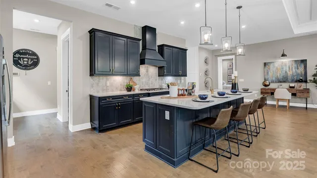 a kitchen with stainless steel appliances granite countertop a refrigerator a sink dishwasher a stove and a dining table with wooden floor