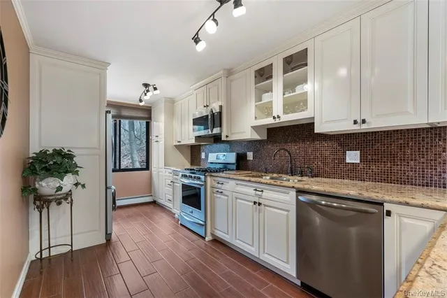 a kitchen with stainless steel appliances granite countertop a stove a sink dishwasher a refrigerator and white cabinets with wooden floor