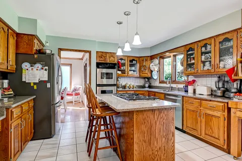 a kitchen with stainless steel appliances granite countertop a stove top oven a refrigerator a sink dishwasher and a dining table with the living room view