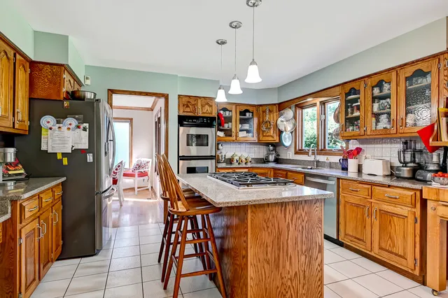 a kitchen with stainless steel appliances granite countertop a stove top oven a refrigerator a sink dishwasher and a dining table with the living room view
