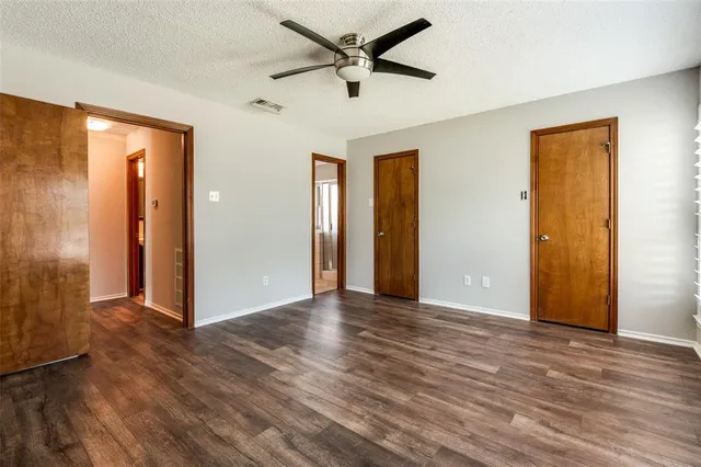 a view of an empty room with wooden floor and a ceiling fan
