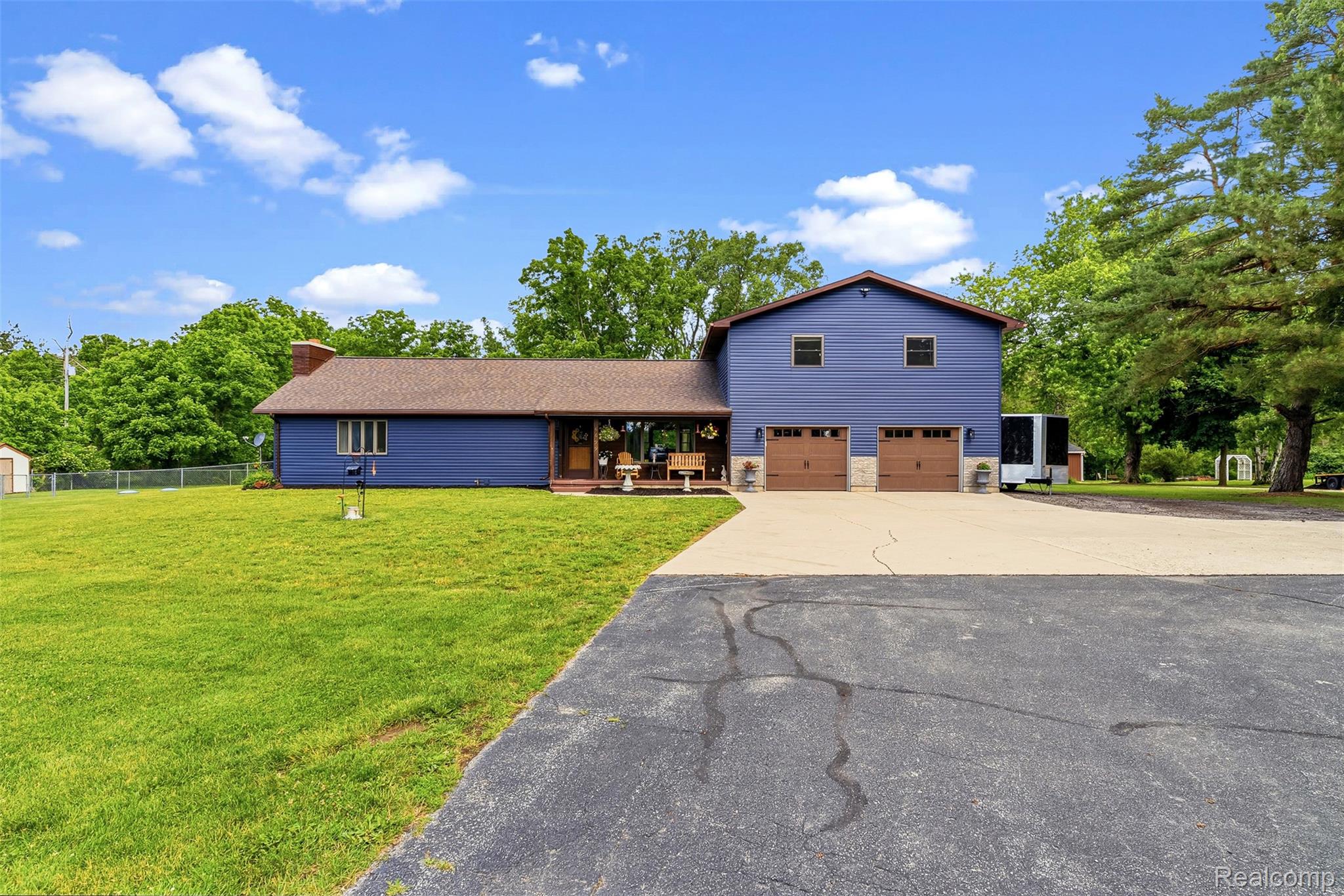 6699 Lansing Road Durand, MI 48429 - Photo 4 of 53 Spacious property featuring a blue siding exterior with a brown shingle roof, a two-car attached garage with wood-finish doors, an expansive paved driveway, and a large front lawn