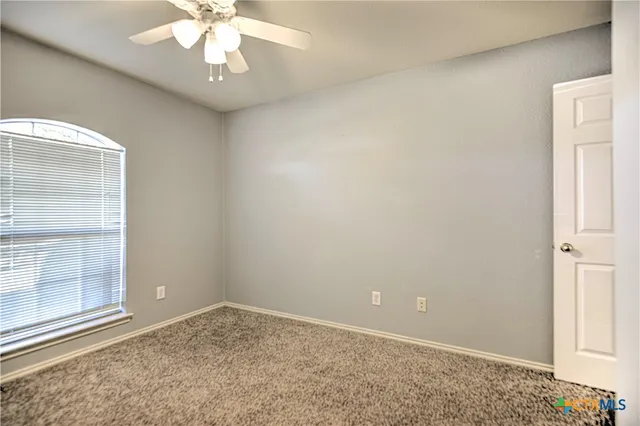 an empty room with a chandelier fan and windows